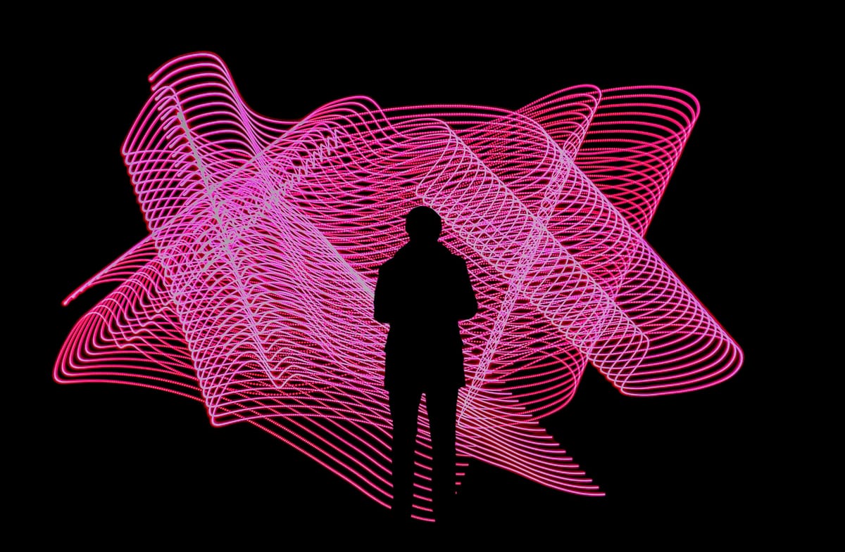 A person stands in front of an art installation showing a swirl of pink lines. Photonic is a distributed quantum computing company.