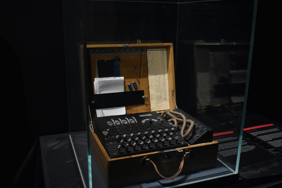 An Enigma encryption machine sits behind a glass case at a museum