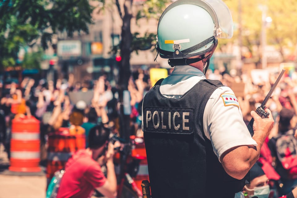 A police officer holding a walkie talkie while overlooking a large crowd. Law enforcement is one of the primary use cases for the TETRA radio protocol