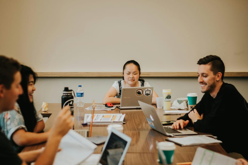 A group of people sit looking at laptops around a table, in a startup meeting
