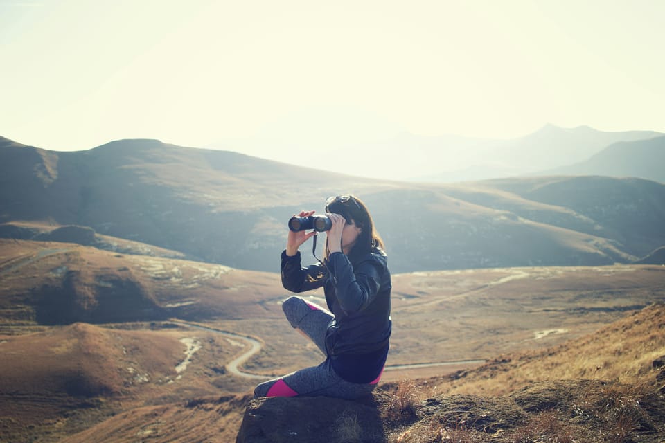 A woman looks out with binoculars while sat on a hill. MongoDB has made its search and vector search tools available in public preview.