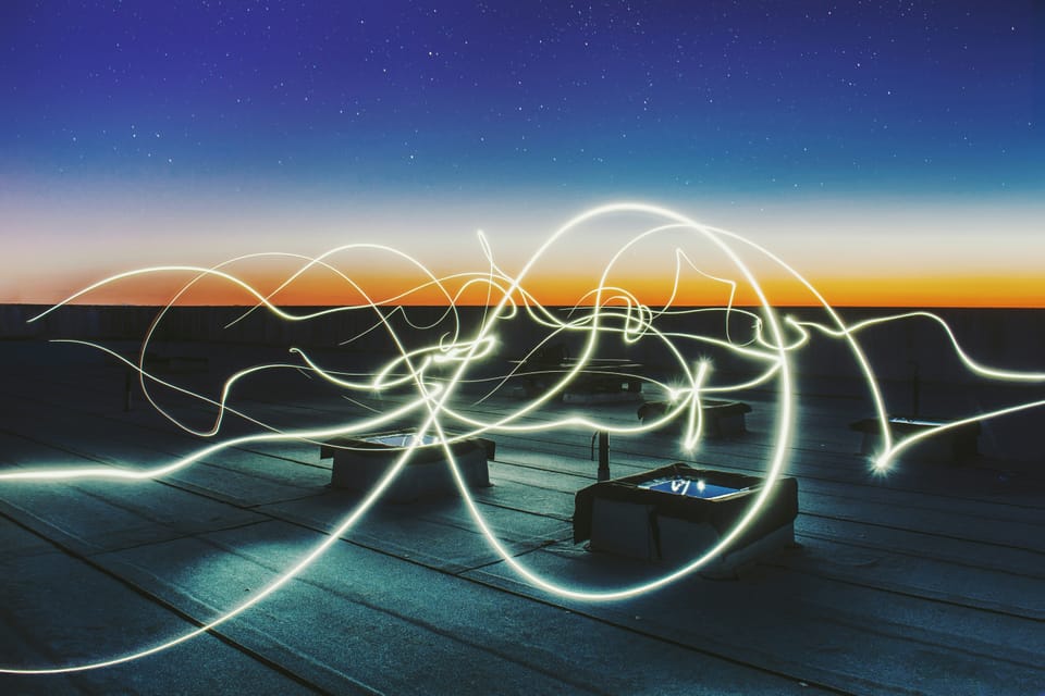 Beams of light swirl across a rooftop with the sunset in the background. Optalysys is a photonic computing startup.