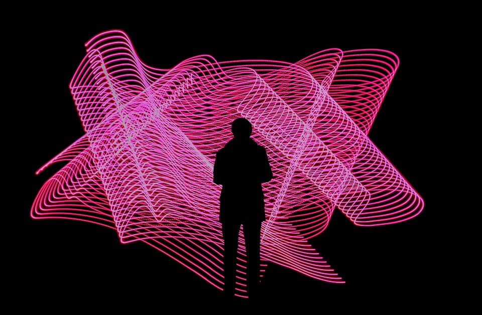 A person stands in front of an art installation showing a swirl of pink lines. Photonic is a distributed quantum computing company.